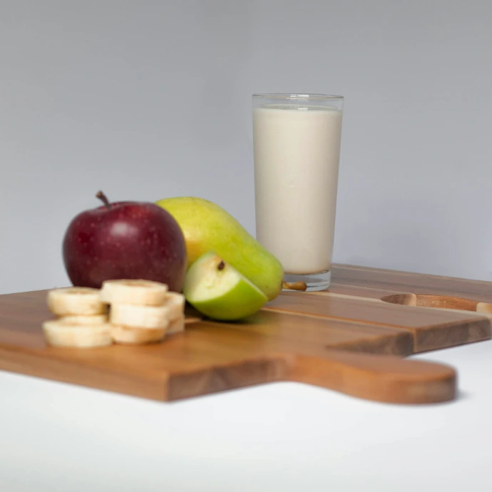a wooden cutting board topped with apples next to a glass of milk